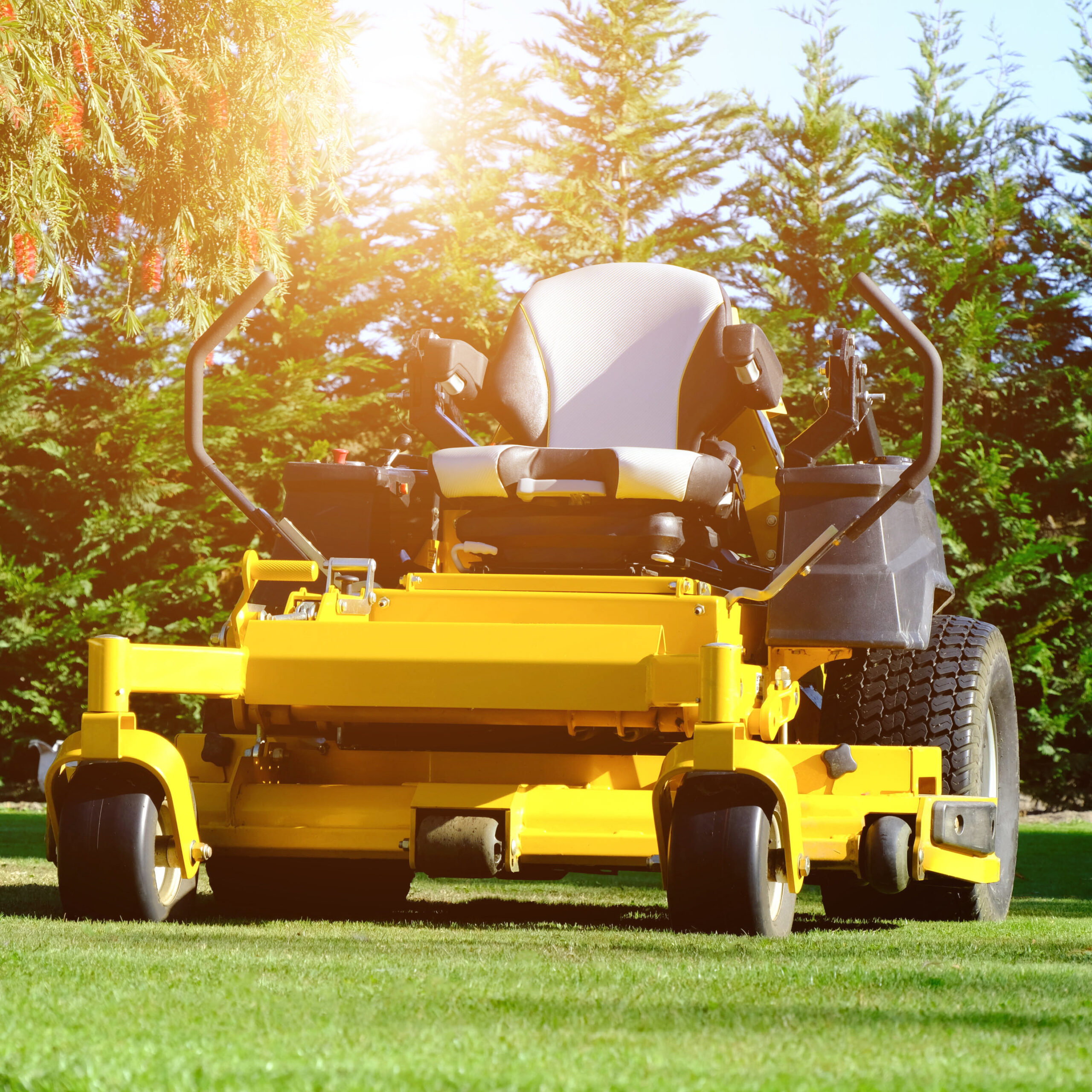 Yellow mower parked in the middle of the green grass field, the orange sunlight splashes behind and the green background fence, mow the lawn service.